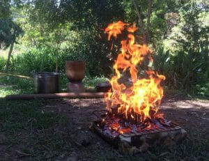 place in naurture with a fire in the foreground and tools in the background, burnig if bark for bashanawu ash